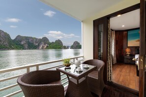 A balcony with wicker chairs, a table, and a view of a river and mountains.
