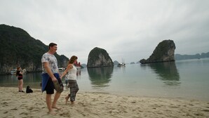 A beach with people walking, boats in the water, and limestone karsts in the background. - Huong Hai Sealife Cruise (Hong Gai)