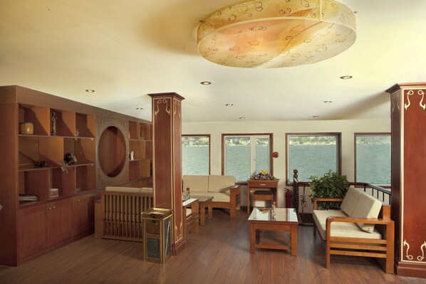 A spacious living room with wooden furniture, a large window overlooking water, and a decorative ceiling light.