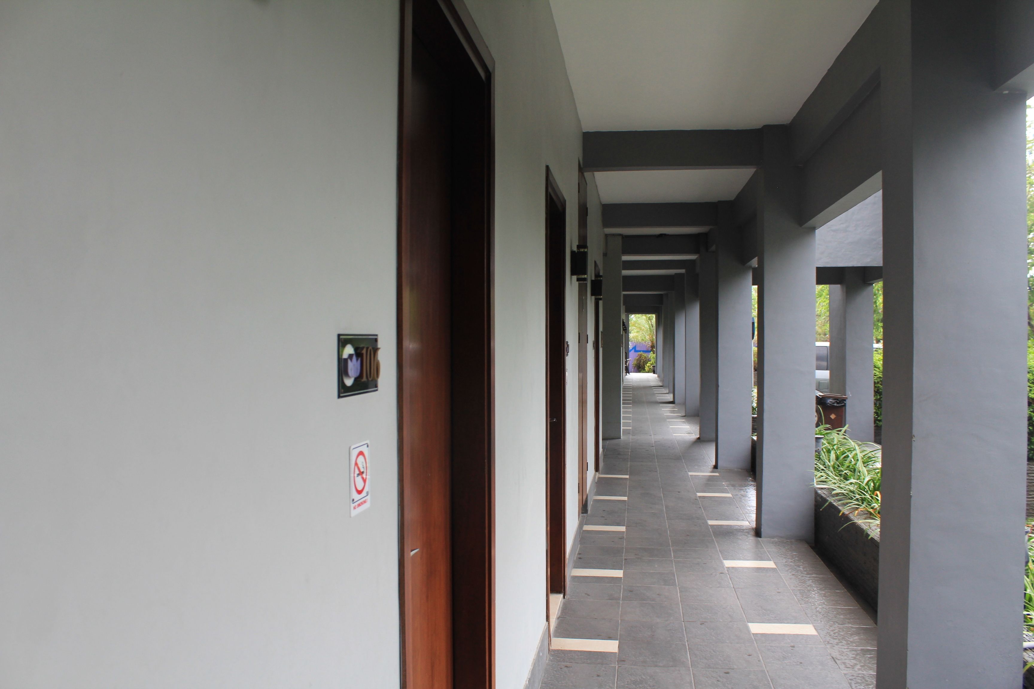 A corridor with a tiled floor, wooden doors, and a no-smoking sign.