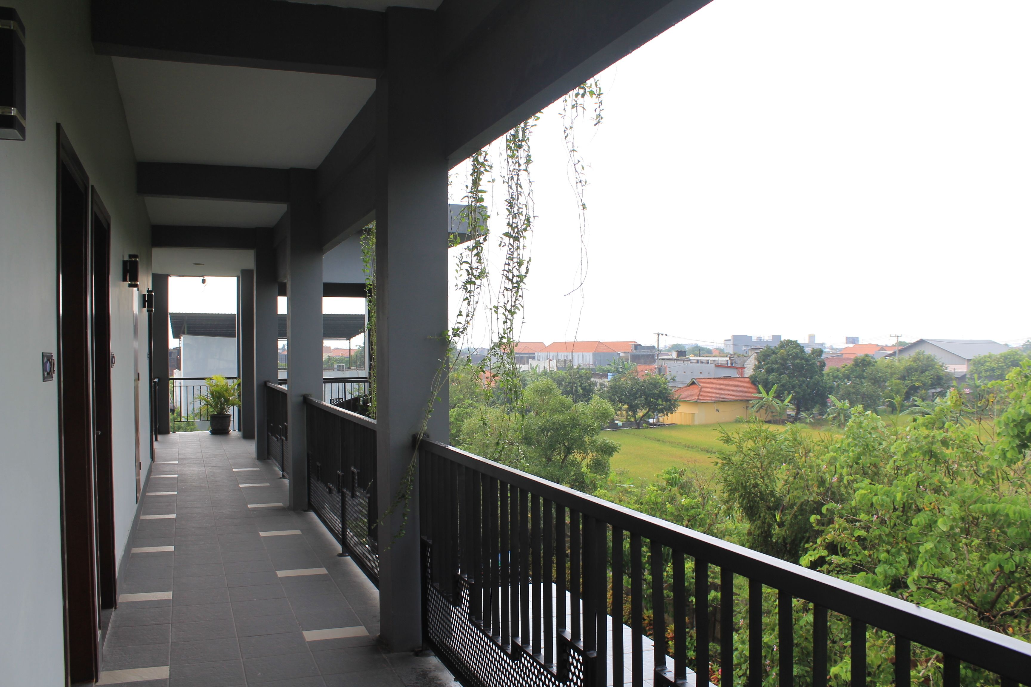 A covered balcony with a view of a green landscape and buildings in the distance.