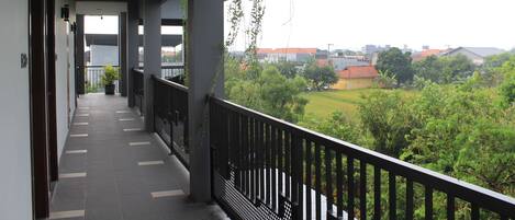 A covered balcony with a view of a green landscape and buildings in the distance.