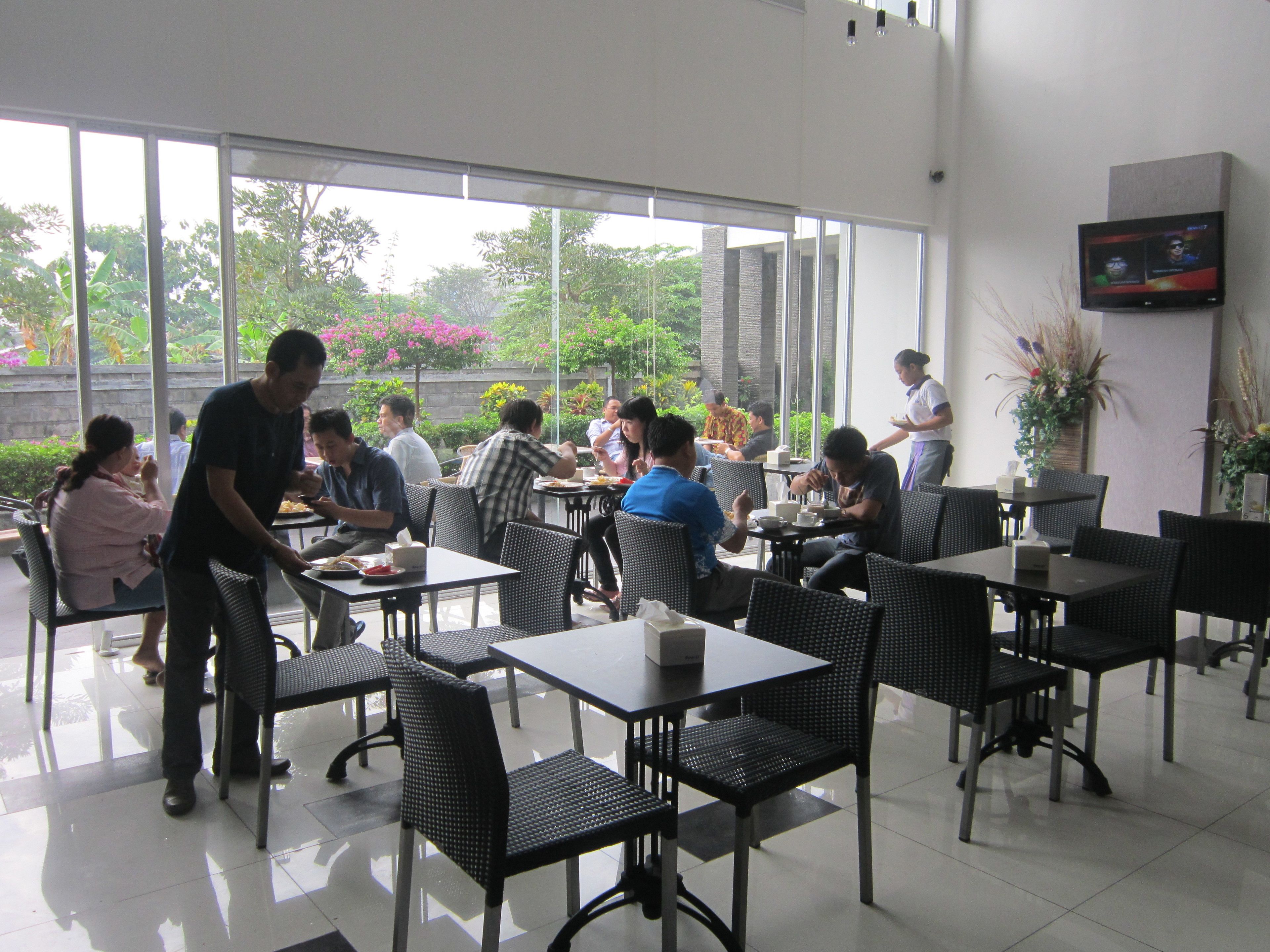 A restaurant with indoor seating, large windows, and a waiter attending to guests.