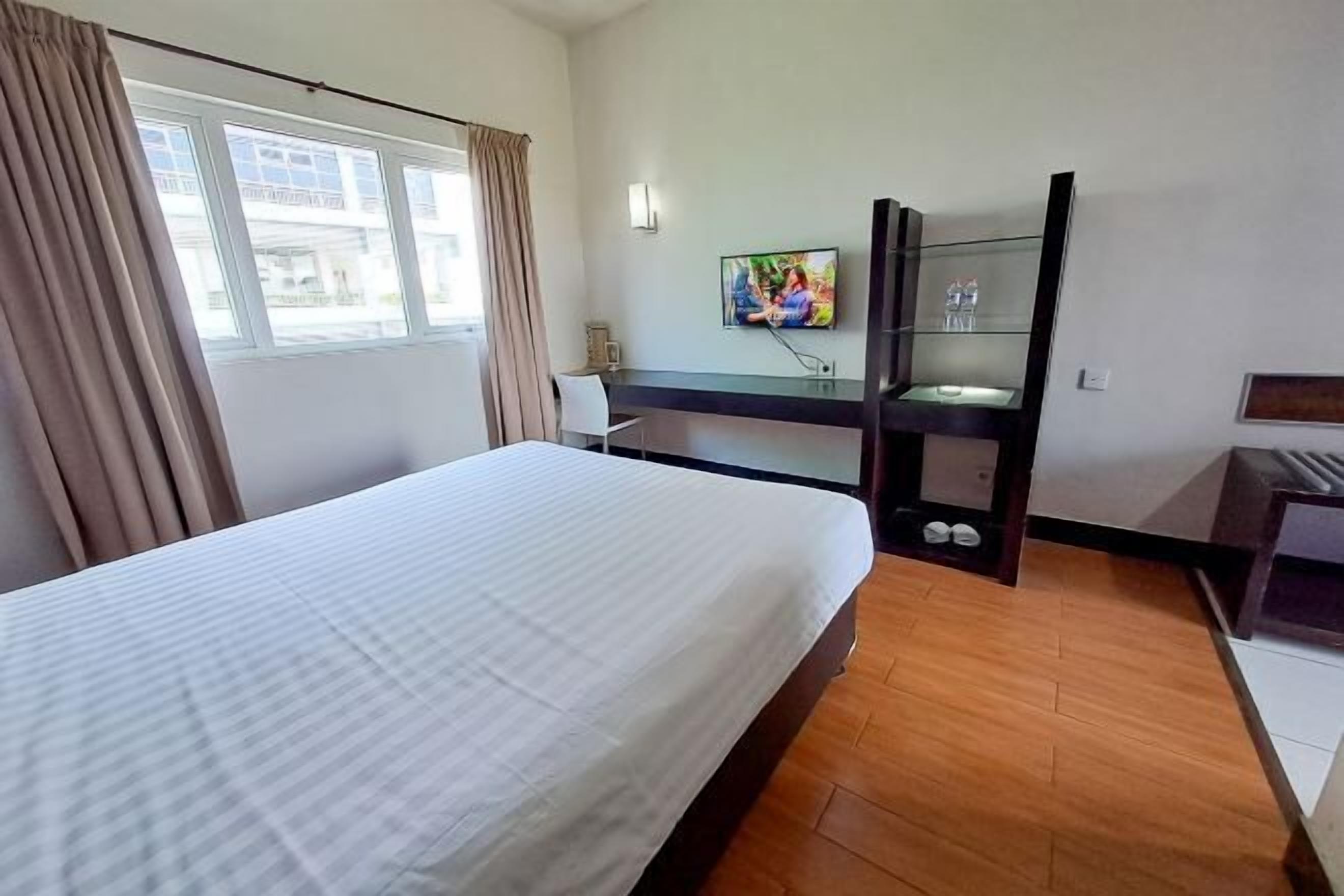 Camera d'albergo con un letto grande, una scrivania con uno specchio, una TV montata a parete e una finestra con tende.