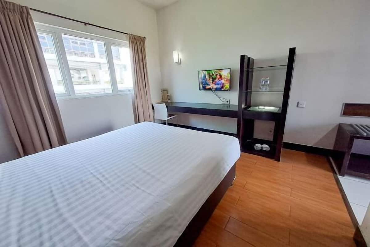 Ett hotellrum med en stor säng, ett skrivbord med en spegel, en tv som är monterad på väggen och ett fönster med gardiner.