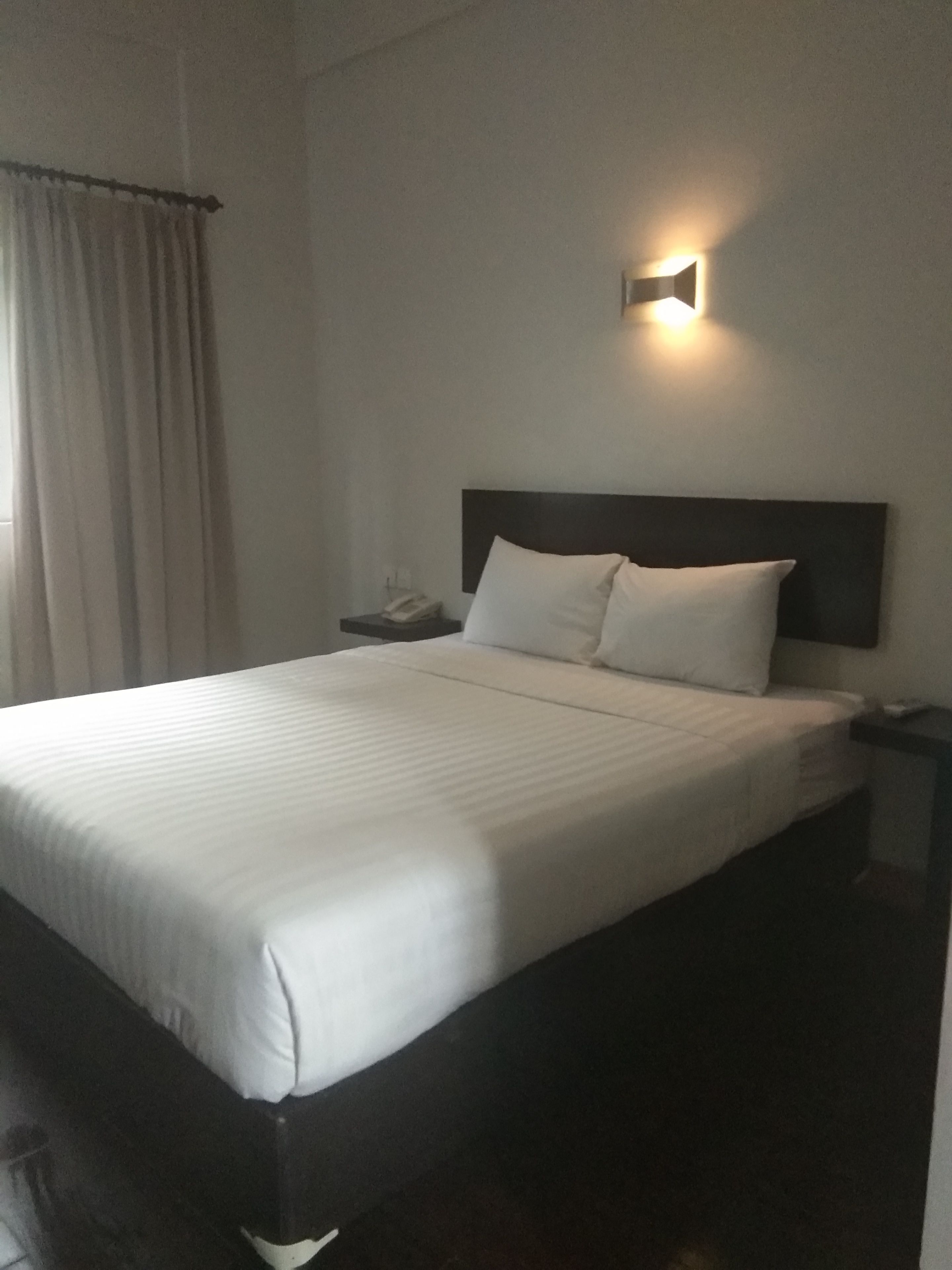 A neatly made bed with white linens, a dark headboard, and a bedside table with a phone.