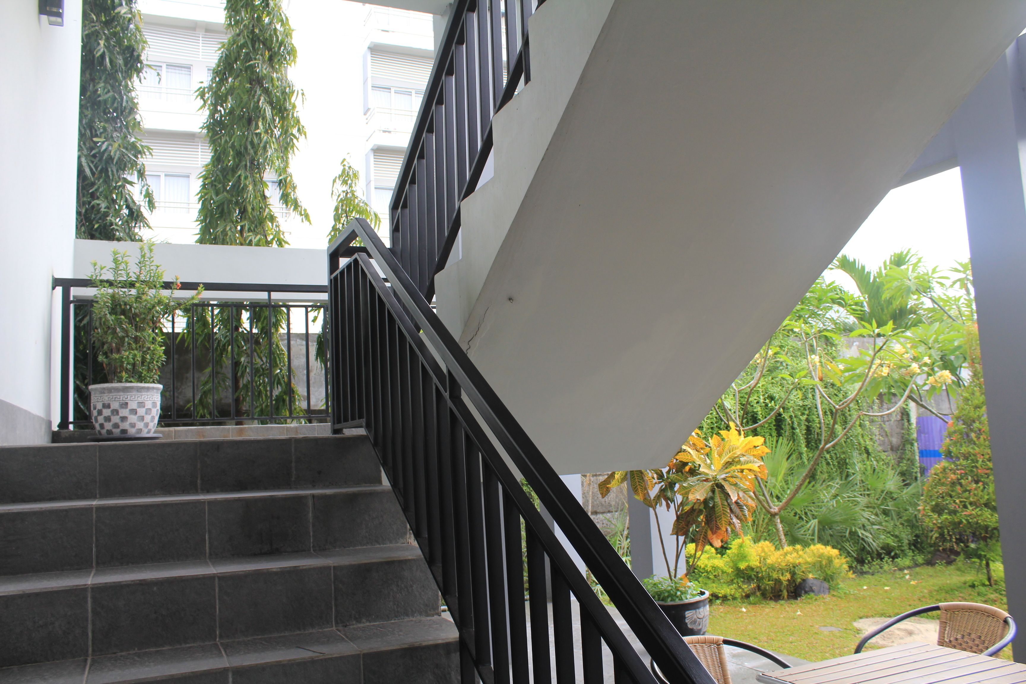A staircase with black railings leading to an outdoor area with potted plants and a view of greenery.