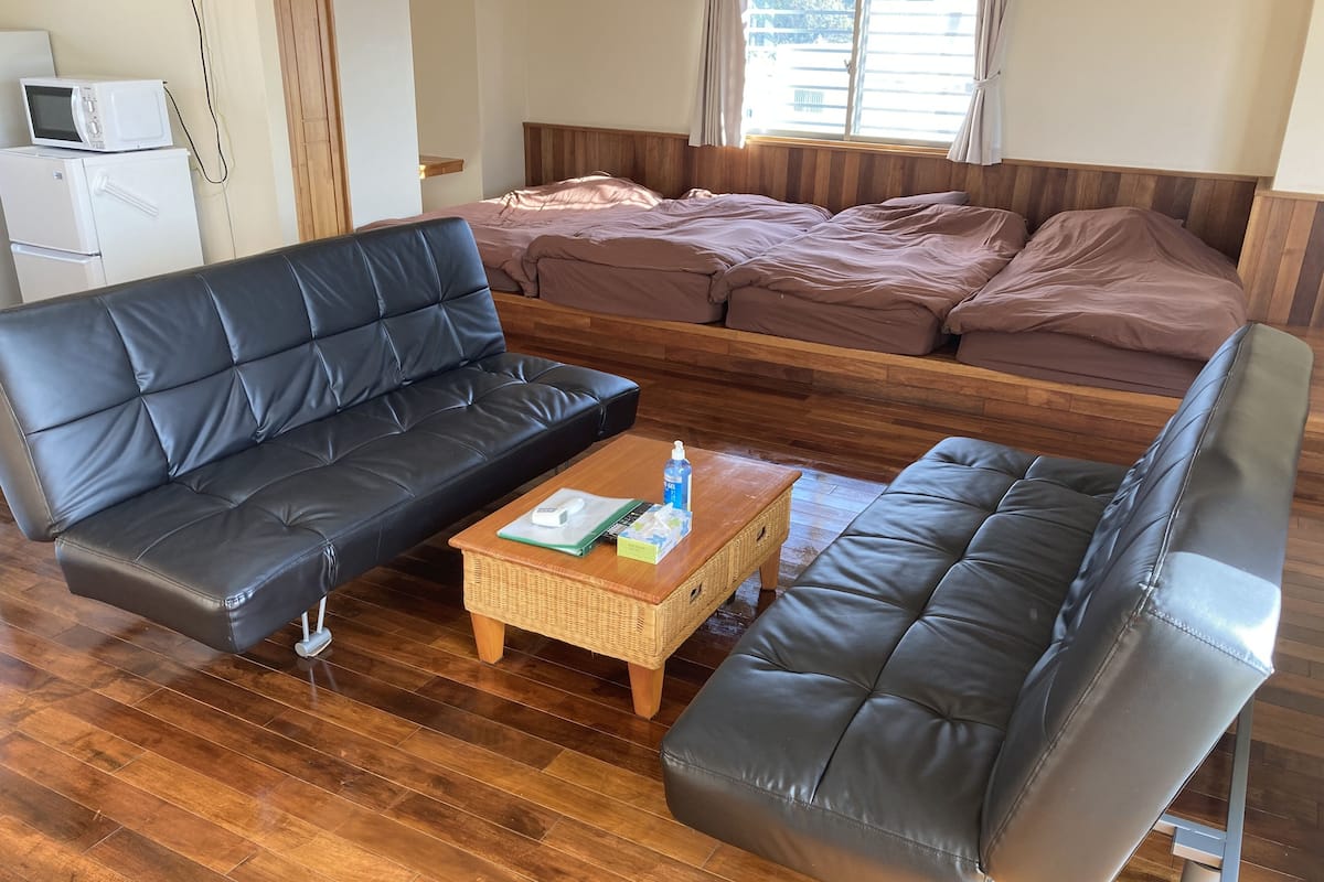 A room with a black leather sofa, a wooden coffee table with a remote control, and a bed with wooden headboard.