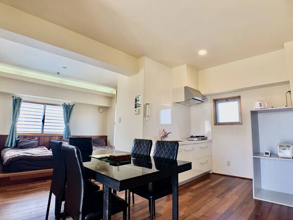 A compact room with a bed, a dining table with chairs, a kitchenette, and a small shelf. - rob cond (Naha)