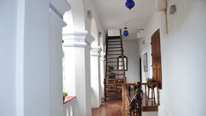 A narrow hallway with white walls and wooden floors, leading to a staircase with a wooden railing and a blue lantern above. - The Old Courtyard Hotel (Kochi)