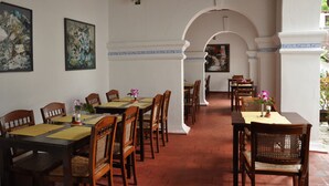 A dining area with multiple tables and chairs, white walls with blue trim, and framed artwork on the walls. - The Old Courtyard Hotel (Kochi)