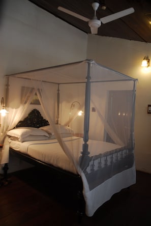 Una cama con dosel y cuatro columnas, con estructura de madera y ropa de cama blanca.