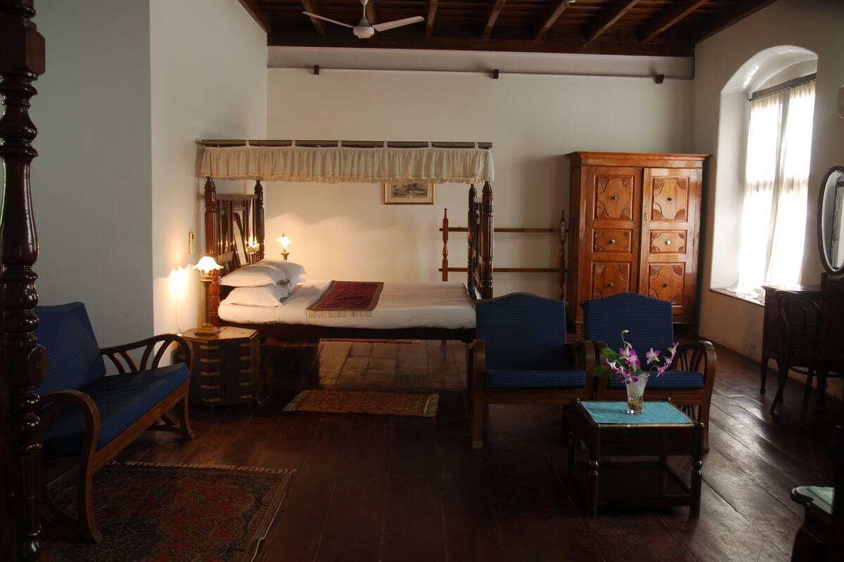 A traditional room with a wooden bed, a nightstand, a chair, a cabinet, and a small table with a vase.