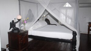 A four-poster bed with a canopy, a small bedside table with a lamp, and a vase with flowers. - The Old Courtyard Hotel (Kochi)