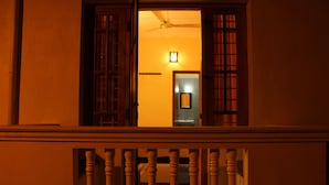 Vista desde un balcón con barandilla de madera, un ventilador de techo y un interior iluminado visible a través de una puerta abierta.