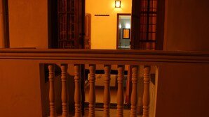 Una escalera con barandilla de madera y vista a un espacio interior con una puerta y una lámpara fijada a la pared.