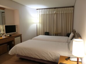 A hotel room with a bed, a desk with a computer, a lamp, and a telephone. - Daedong Hotel (Jeju City)