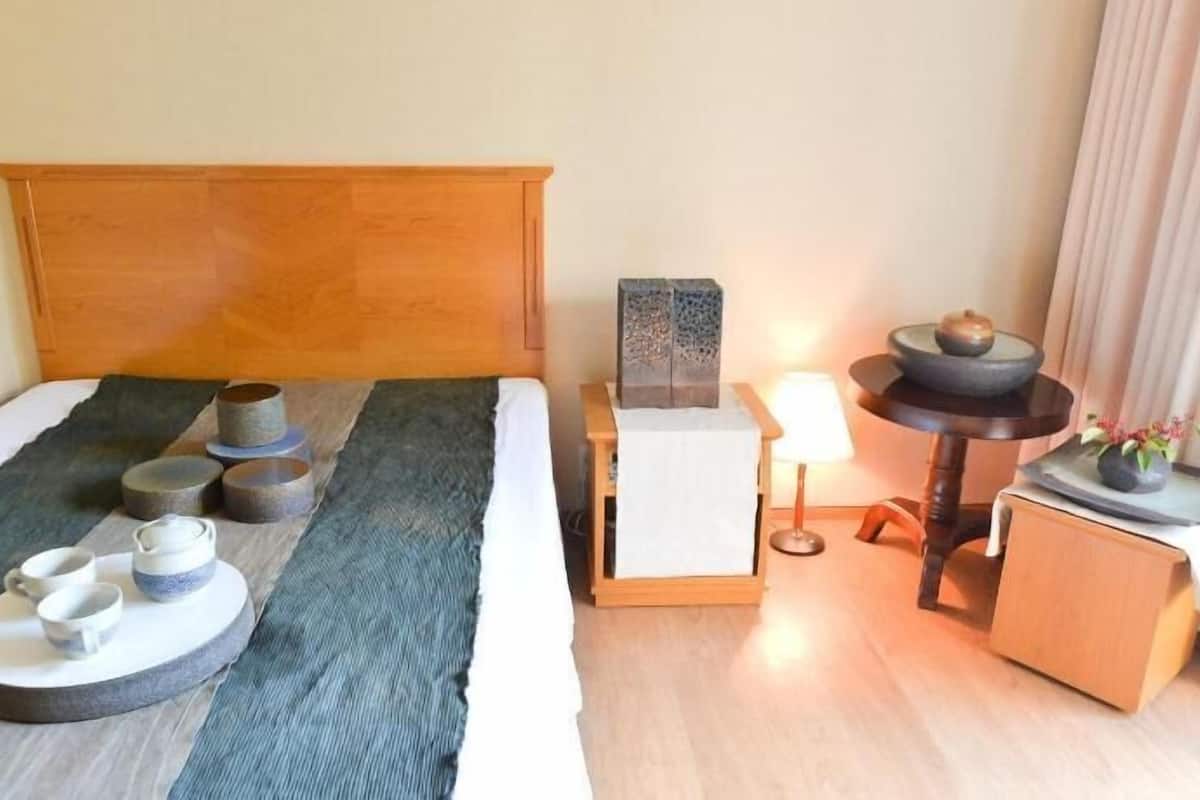 A neatly arranged hotel room with a bed, bedside table, lamp, and a small table with decorative items.