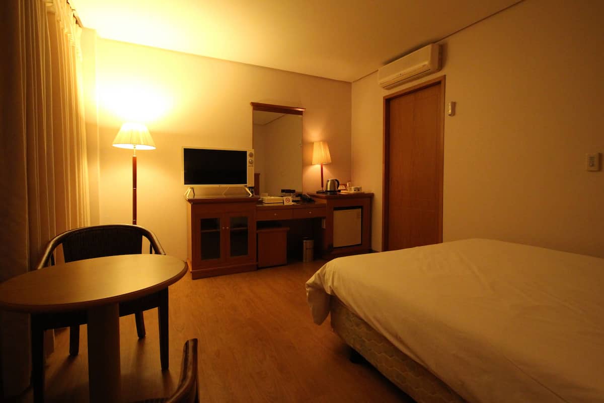 A hotel room with a bed, a desk with a computer, a chair, a lamp, and a television.