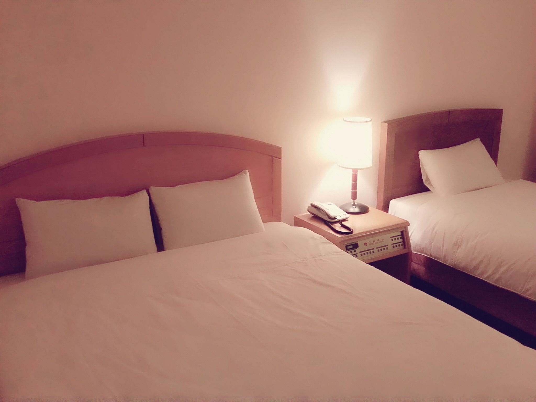 Una habitación de hotel con dos camas, una mesita de noche con lámpara y un teléfono.