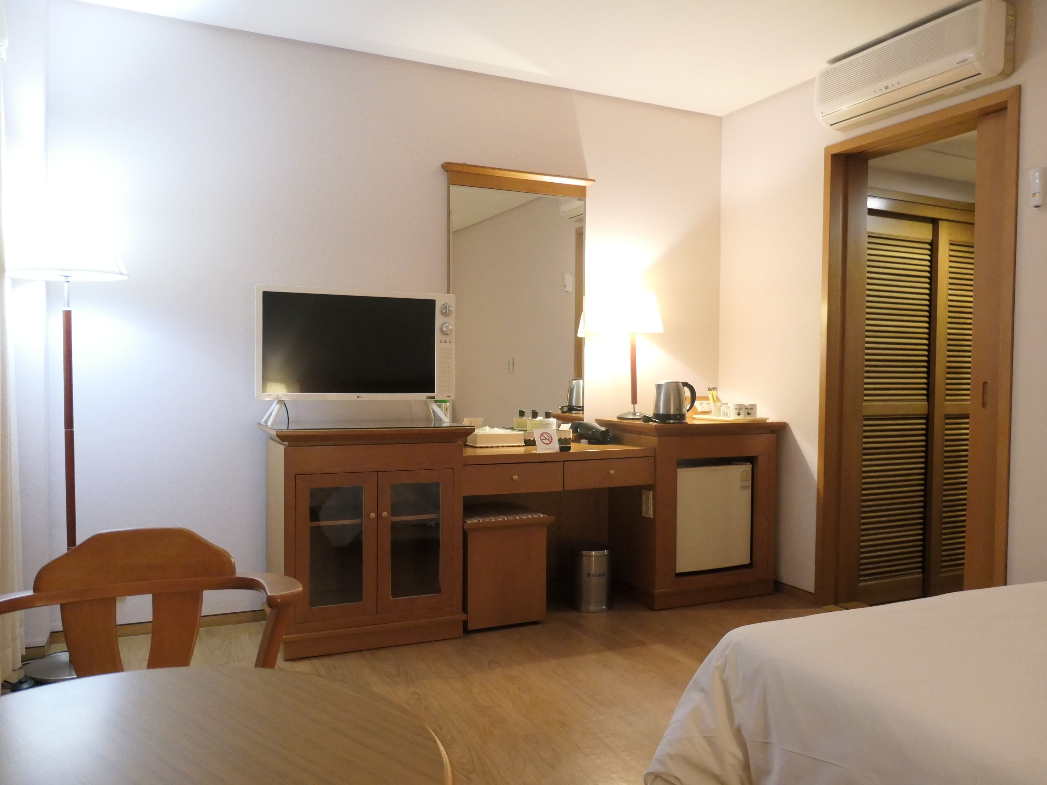 Une chambre d’hôtel équipée d’un bureau en bois, d’une télévision, d’un miroir, d’un mini-réfrigérateur, d’une machine à café et d’un lit.