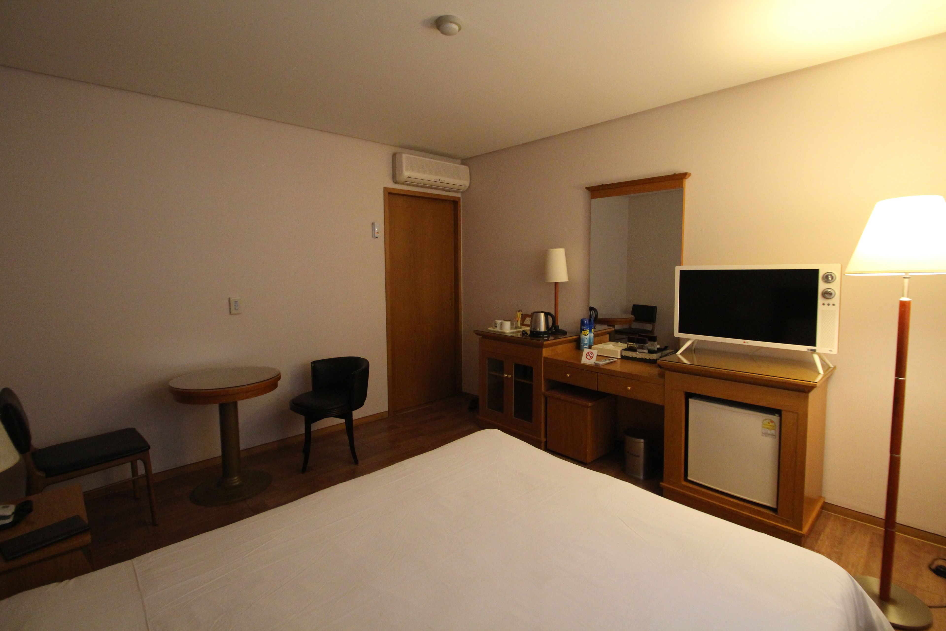 Une chambre d’hôtel comprenant un lit, un bureau avec un ordinateur, une chaise, une petite table, une lampe et un téléviseur.