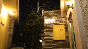 A wooden staircase leading to a building entrance, with a stone wall and a lantern on the right. - Daedong Hotel (Jeju City)