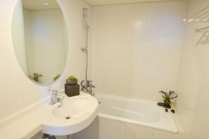 A bathroom with a white sink, a mirror, and a bathtub. - Daedong Hotel (Jeju City)