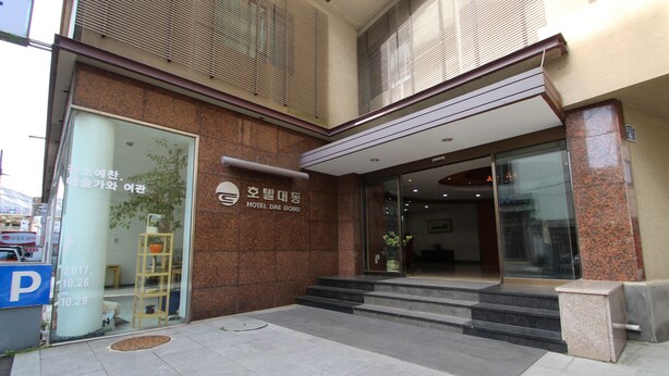 The exterior of Hotel Dae Dong with a clear entrance, steps leading up to the door, and a parking sign visible to the left. - Daedong Hotel (Jeju City)
