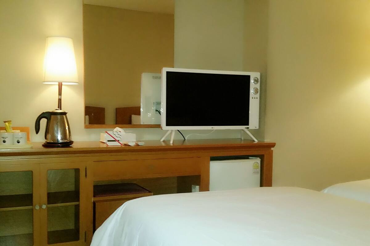 A hotel room with a bed, a desk with a lamp, a coffee maker, and a television.