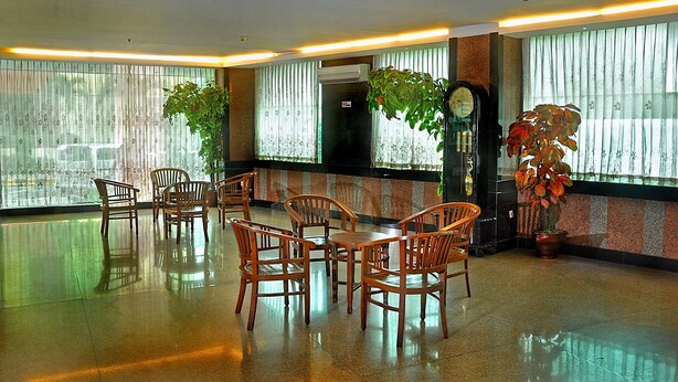 A lobby with a polished floor, wooden chairs and tables, large windows with sheer curtains, and potted plants. - Plaza Hotel Harco Mangga Dua (Jakarta)
