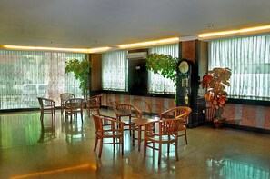 A lobby with a polished floor, wooden chairs and tables, large windows with sheer curtains, and potted plants. - Plaza Hotel Harco Mangga Dua (Jakarta)