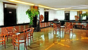 A hotel lobby with a reception desk, several wooden chairs, a large potted plant, and a tiled floor. - Plaza Hotel Harco Mangga Dua (Jakarta)