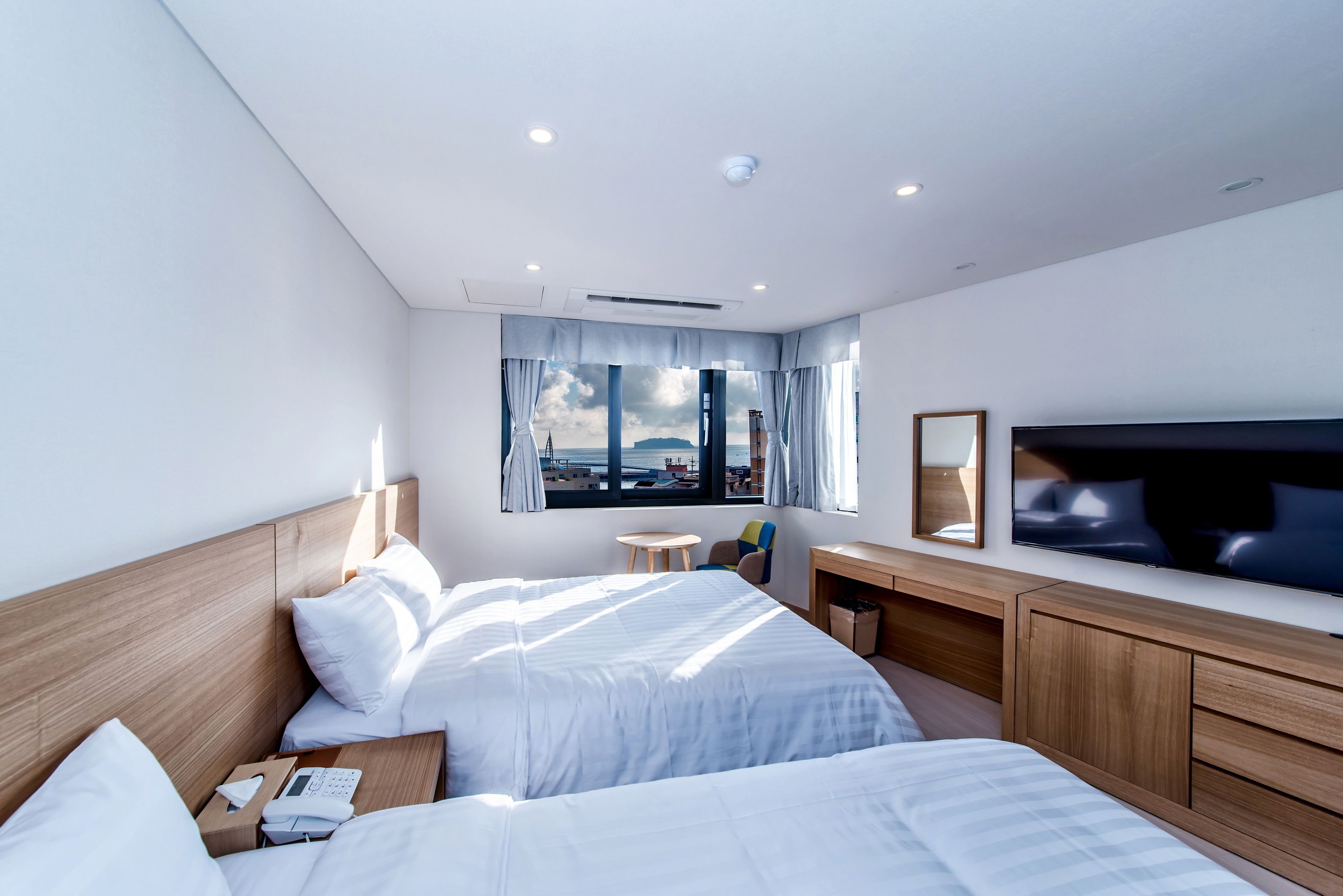 Une chambre d’hôtel moderne avec deux lits, une télévision, un bureau et une grande fenêtre donnant sur un beau paysage.