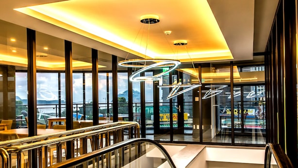 Vista interior de un edificio moderno con una escalera mecánica, barandillas de cristal y vistas al exterior a través de amplios ventanales.