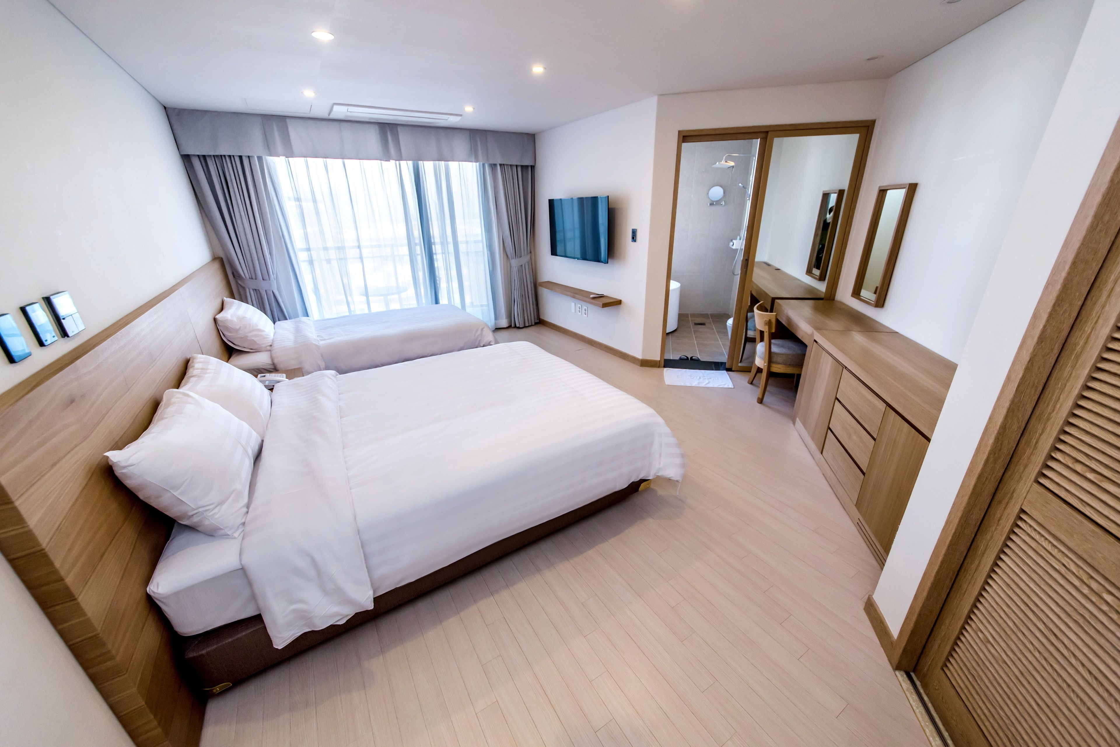 Habitación de hotel con dos camas, televisión, espejo y zona de ducha.