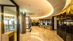 Un interior moderno con mostrador de recepción, zona de estar y fachada de vidrio de un restaurante.
