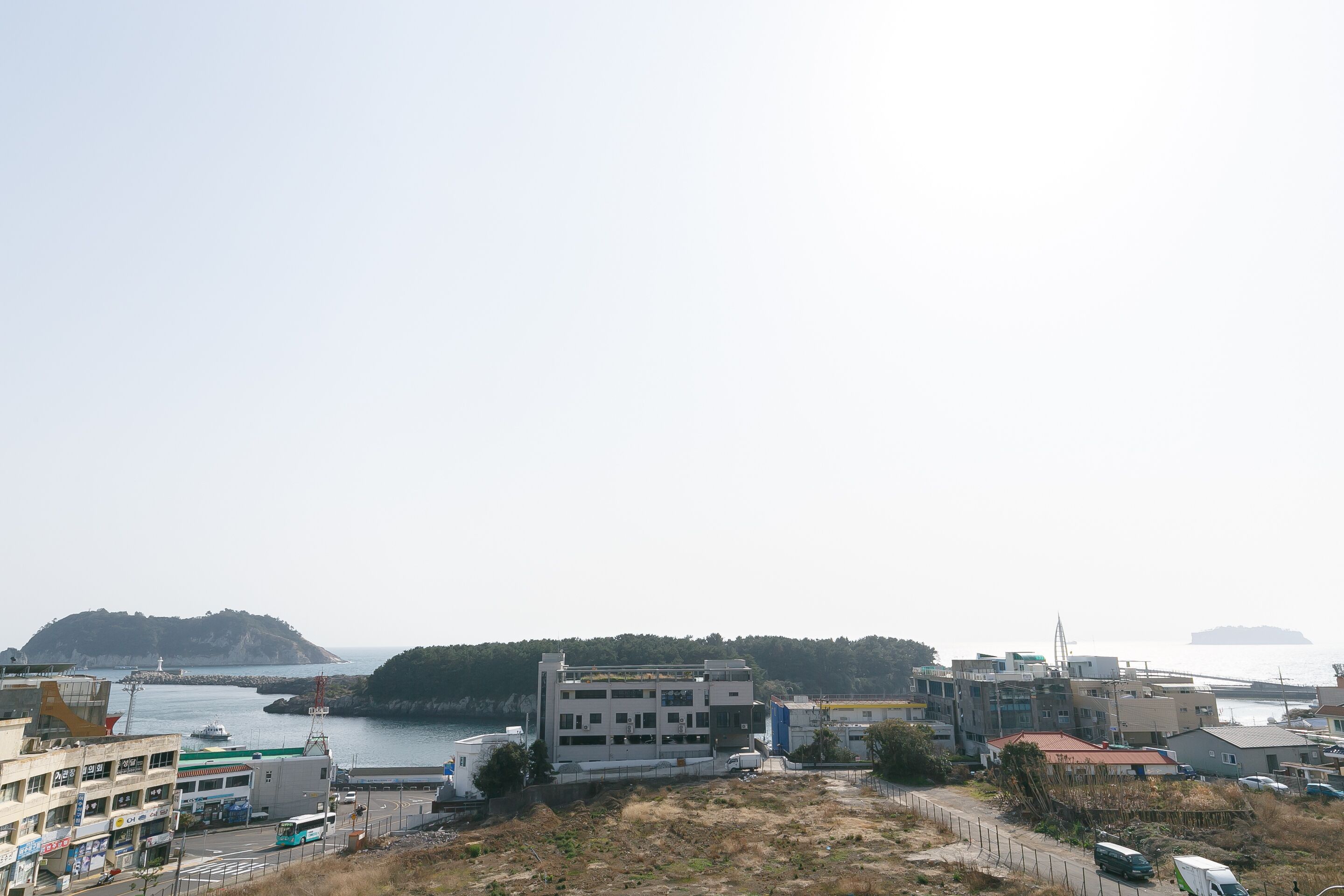 A coastal urban area with modern buildings, a ferry dock, and a hilly island in the background.