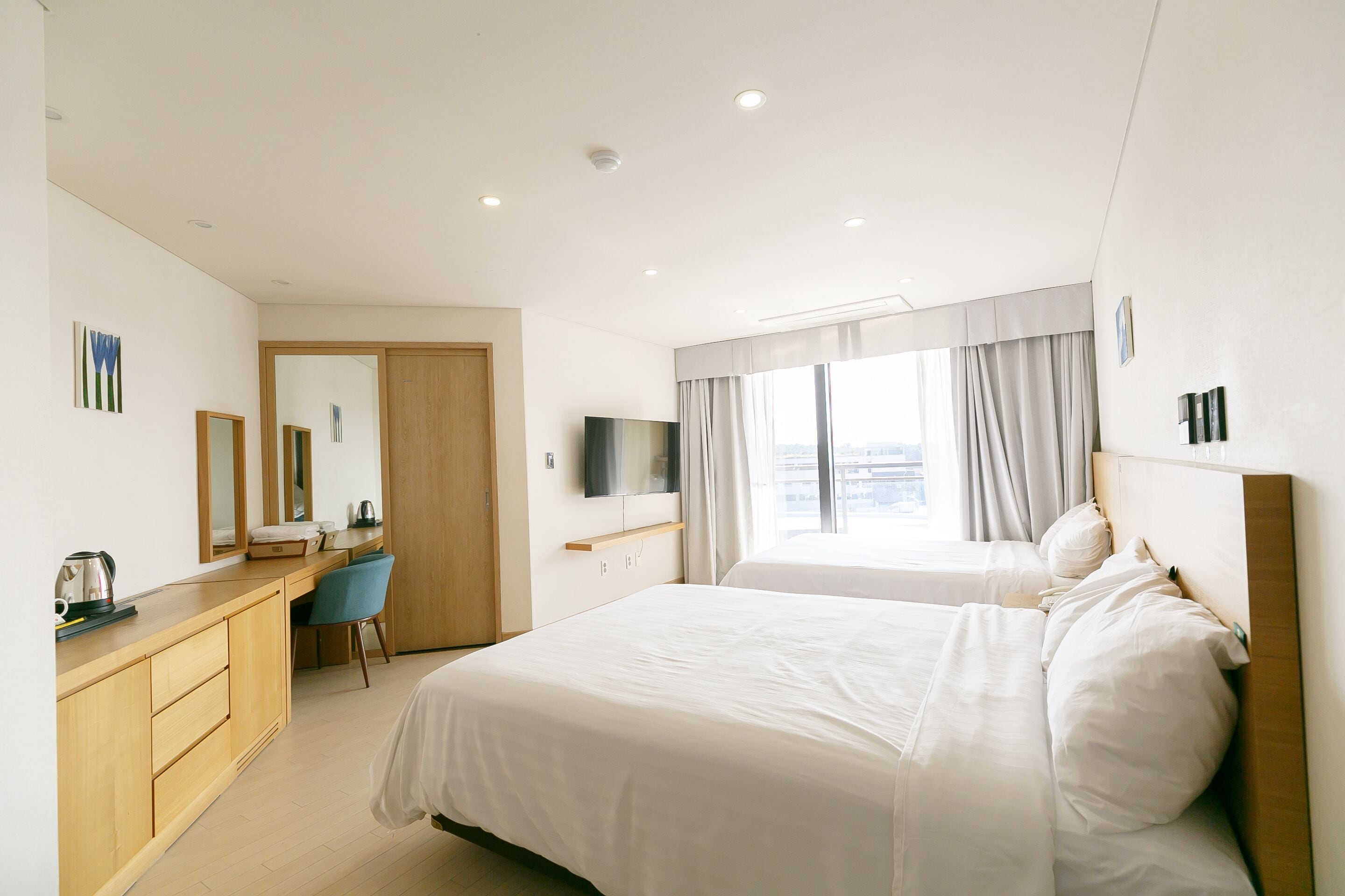 A hotel room with two beds, a desk, a chair, a television, and a large window with curtains.
