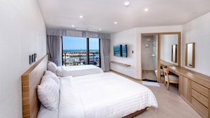 Una habitación de hotel moderna con dos camas, televisión, baño y vista al mar.