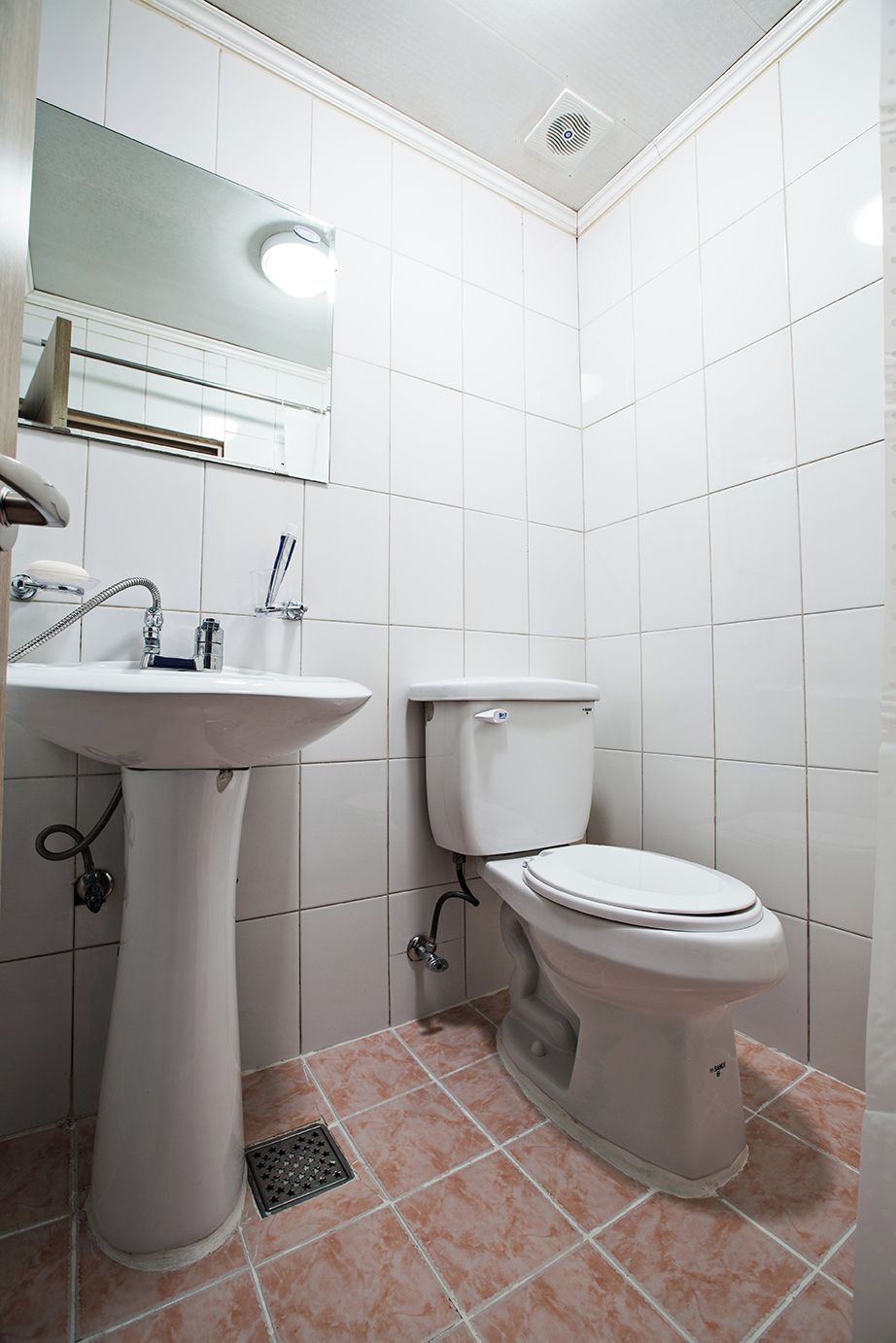 A bathroom with a pedestal sink, a toilet, and a mirror above the sink.