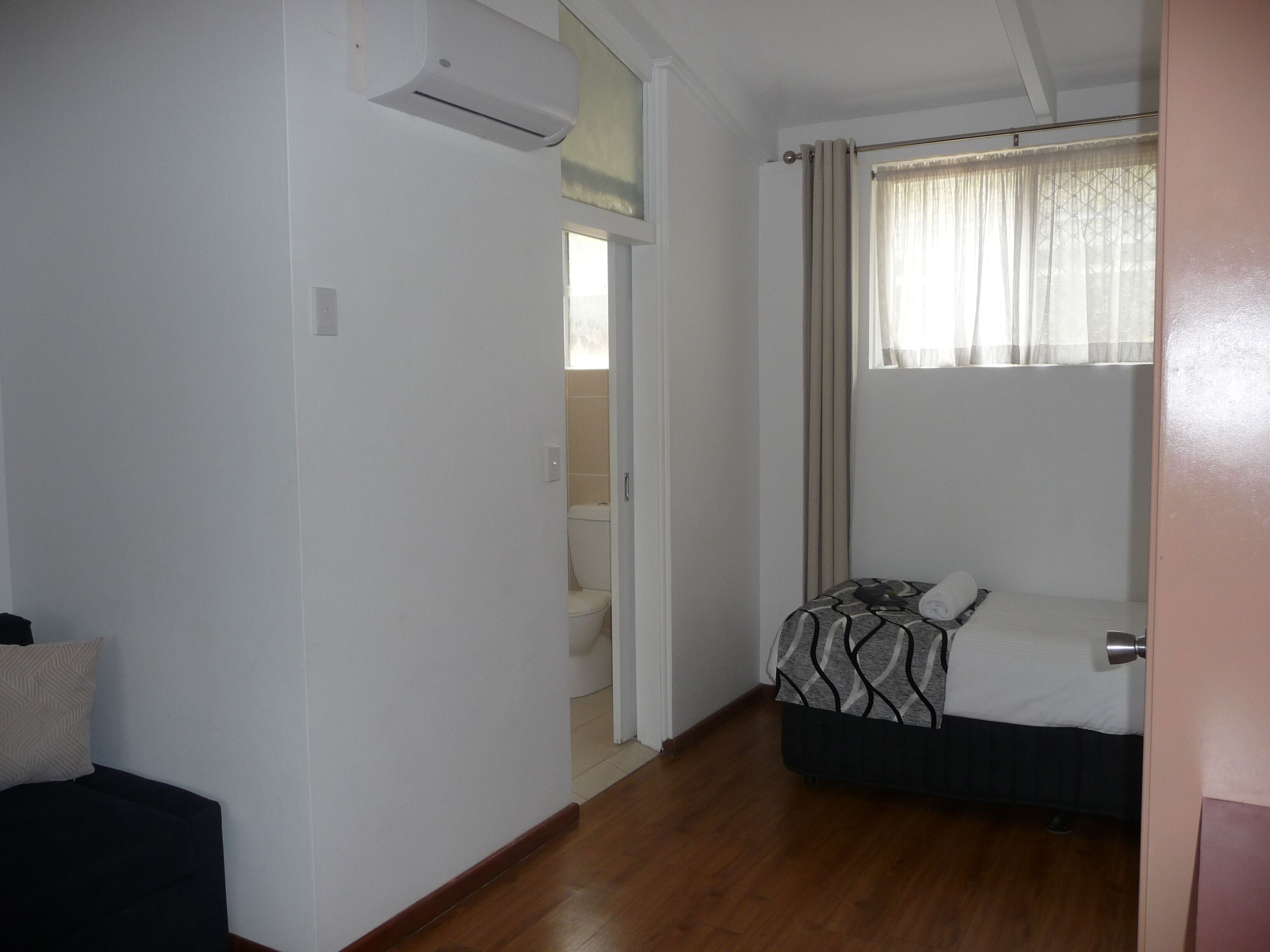 A room with a bed, a window with curtains, a door, and an air conditioning unit.