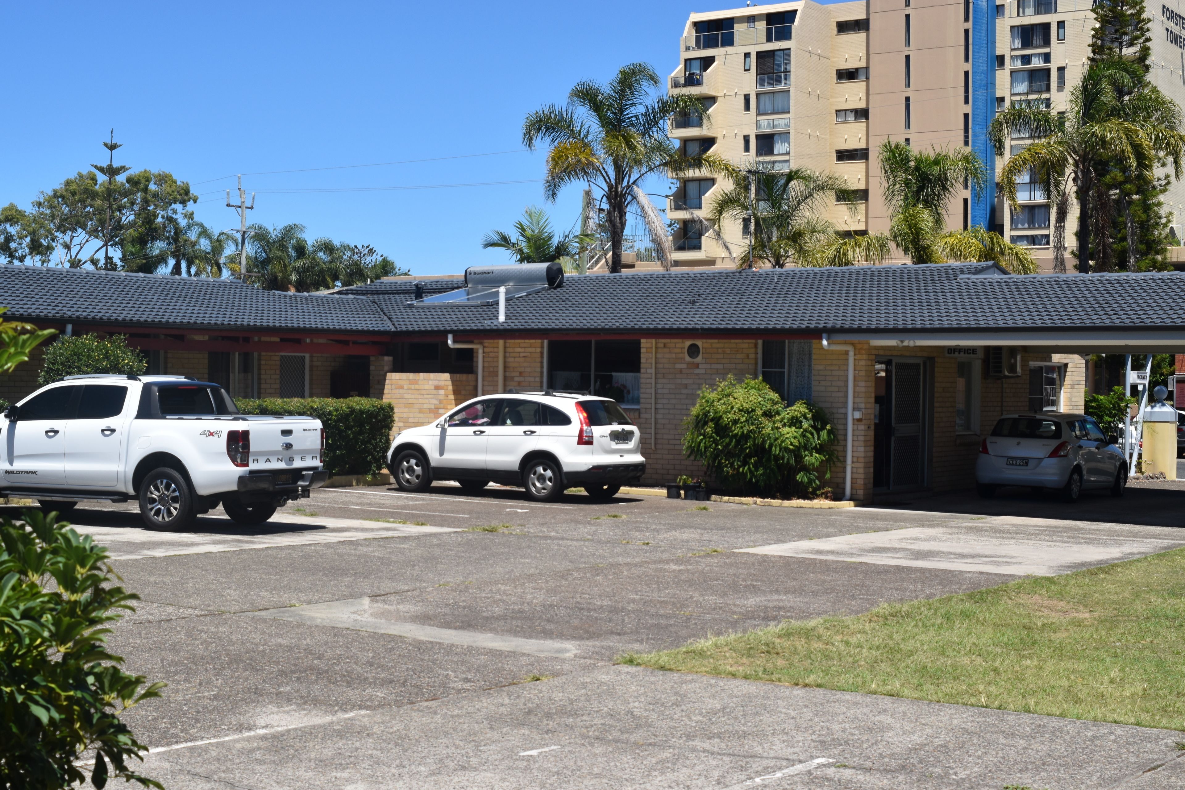 A building with a flat roof, a parking area with two white vehicles, and a small office entrance.