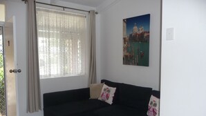 A room with a dark-colored sofa, a window with sheer curtains, and a painting of a cityscape on the wall. - Forster and Wallis Lake Motel (Forster)