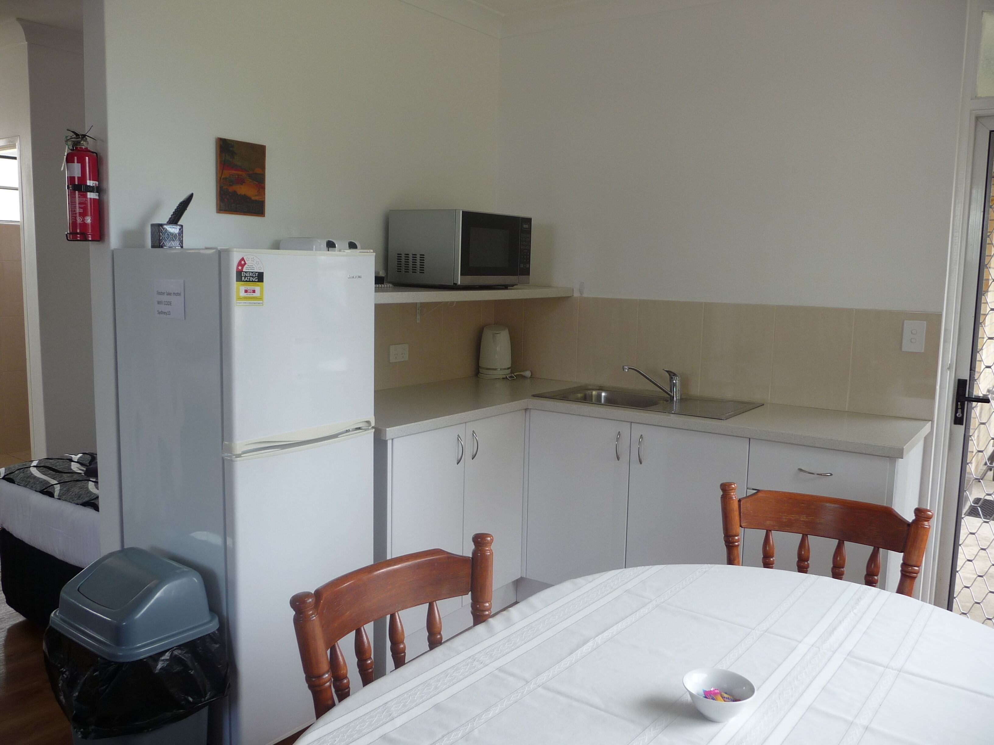 A compact kitchen with a refrigerator, microwave, sink, and wooden chairs around a table.