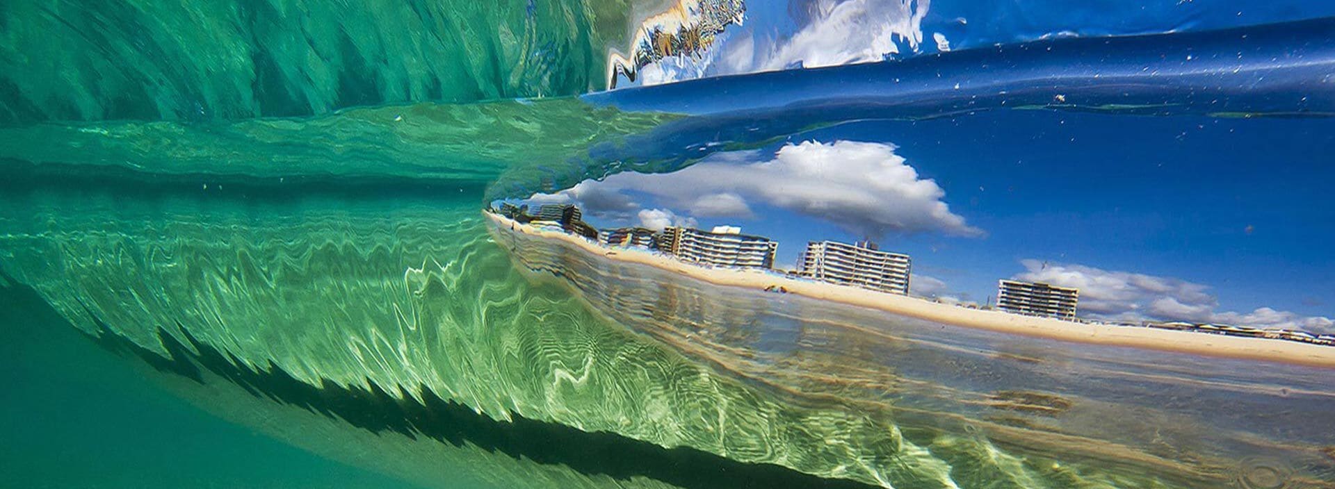 A beachfront hotel with a clear view of the ocean and a large wave.