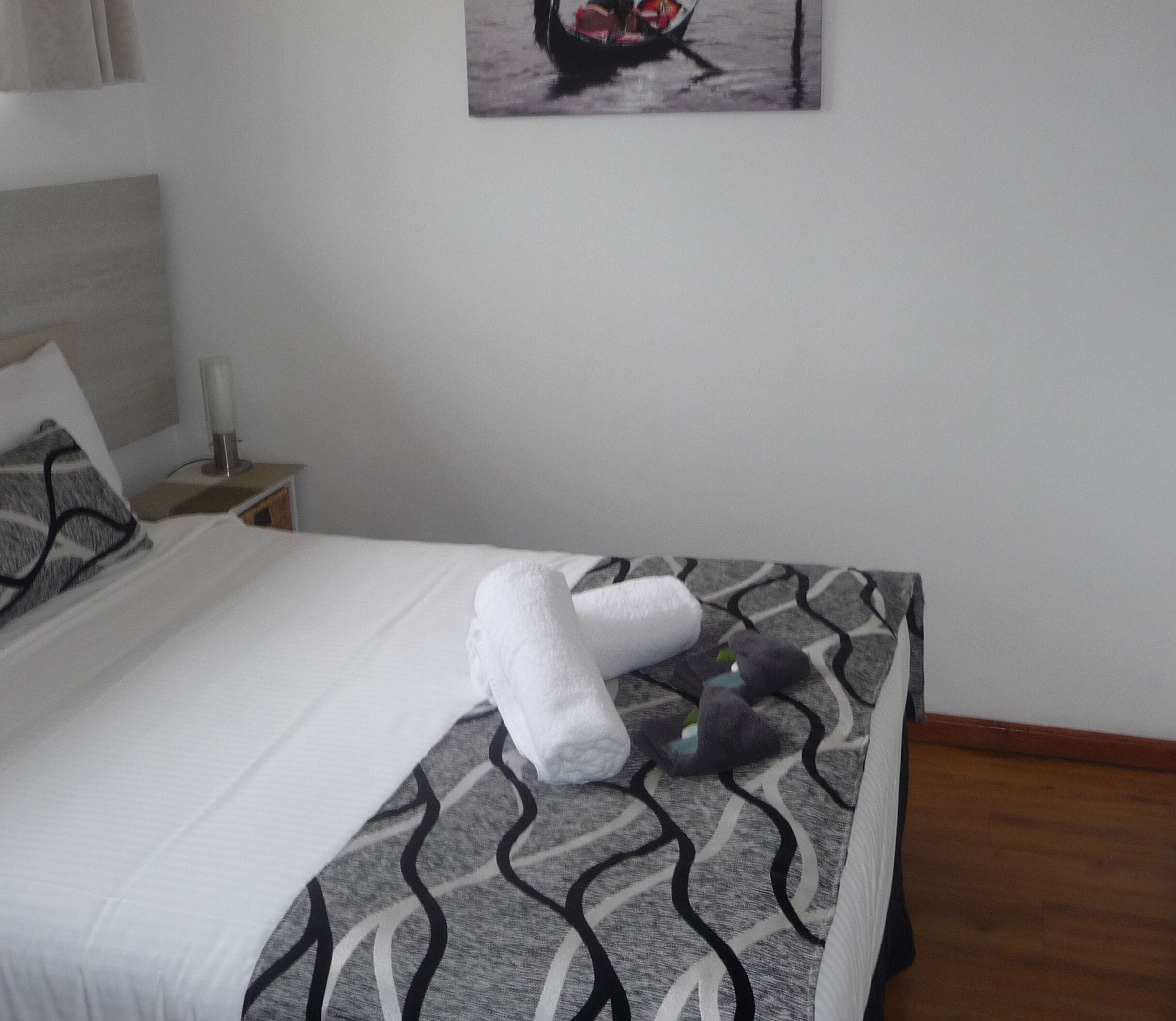 A neatly made bed with a patterned bedspread, a rolled towel, and a decorative pillow.