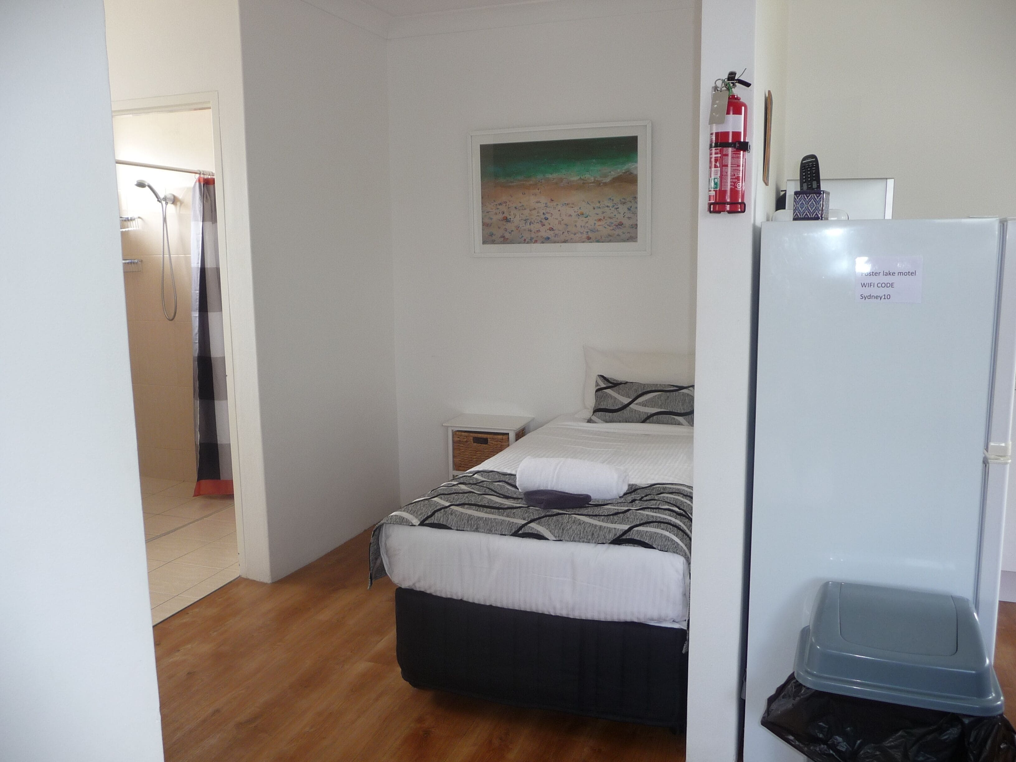 Une chambre à coucher comprenant un lit, une table de chevet, un tableau, un extincteur et un réfrigérateur.