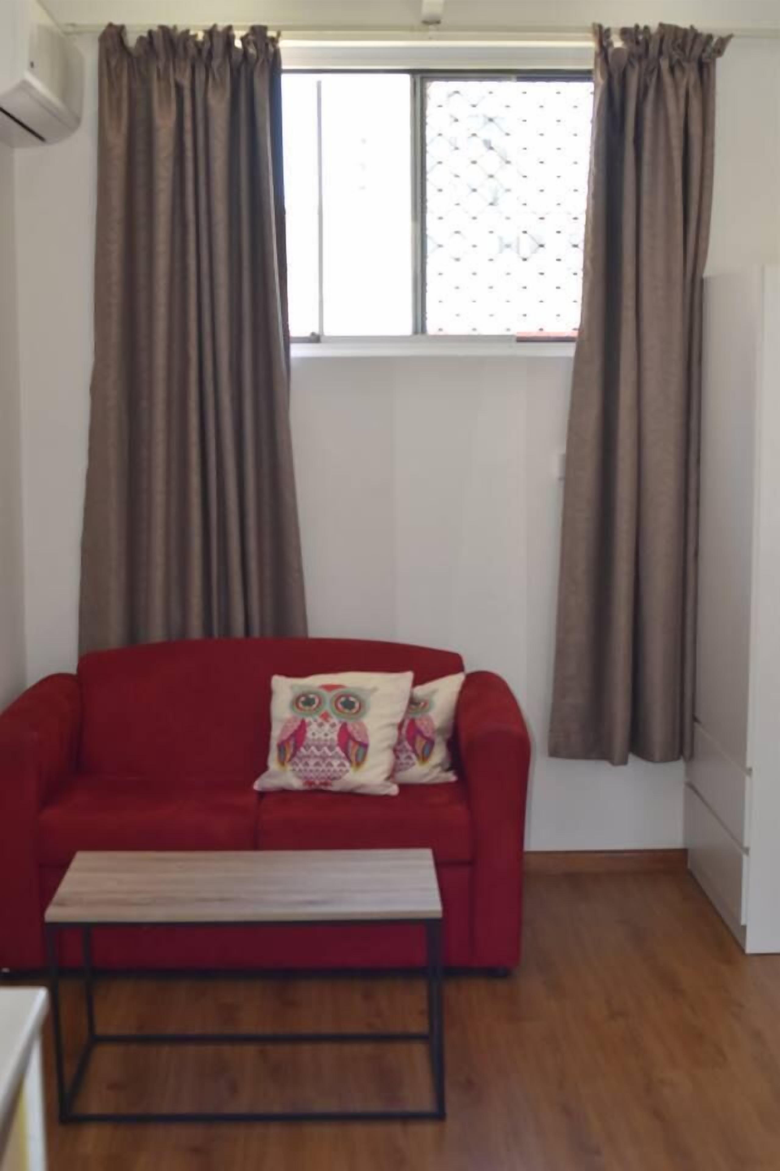 Ein rotes Sofa mit einem gemusterten Kissen, eine hölzerne Bank und ein Fenster mit Vorhängen.