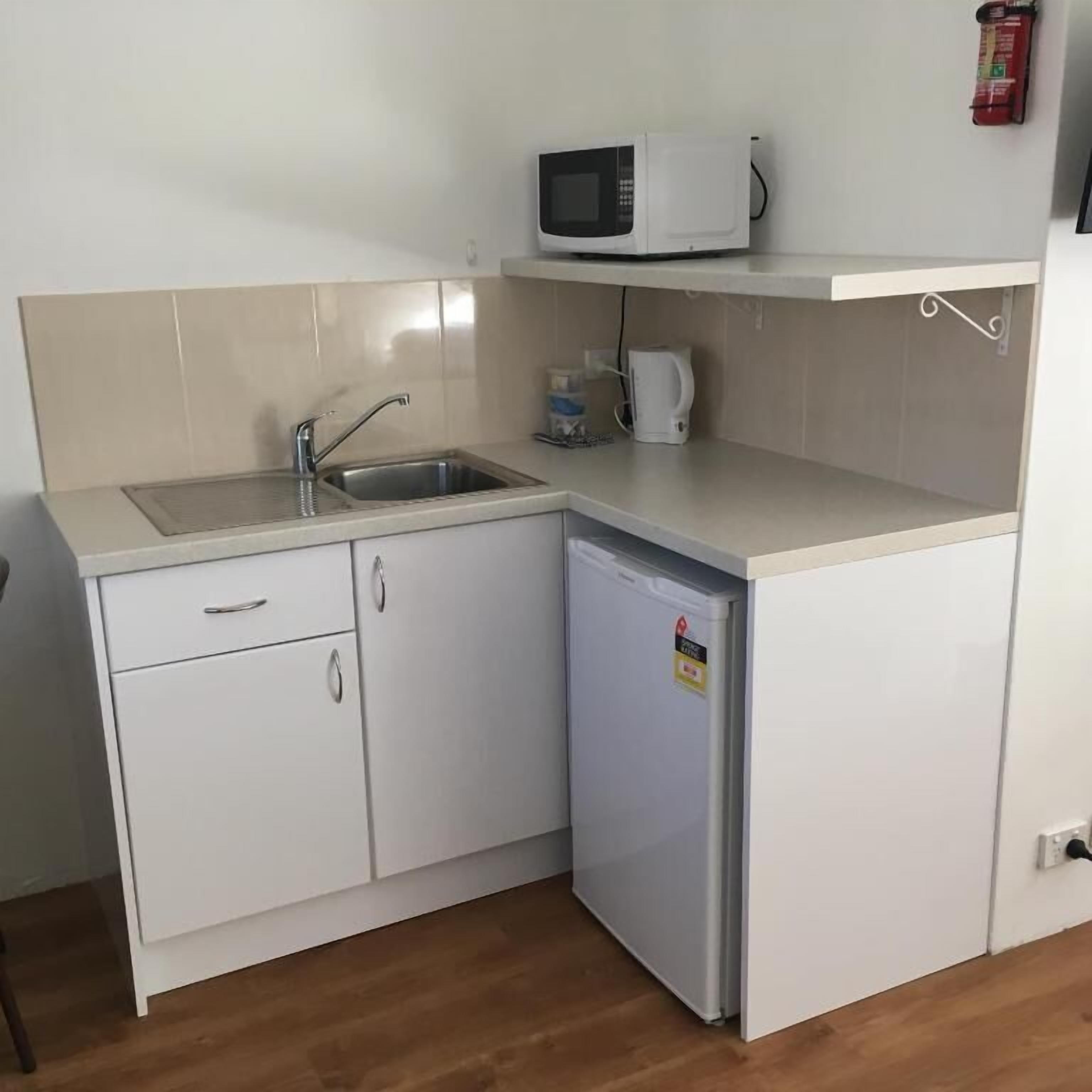 Una cocina compacta con un lavamanos, un microondas y un refrigerador pequeño.